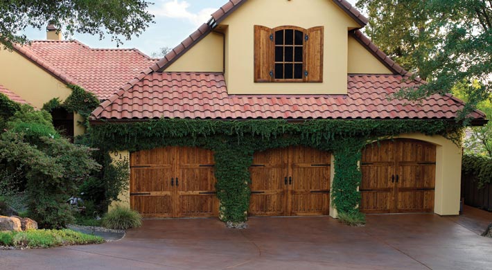 House with stucco siding, villa tile roofing, and three wood carriage house garage doors