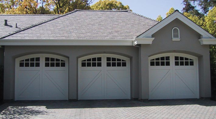 Three car garage with stucco siding and three white carriage house garage doors with no visible hardware
