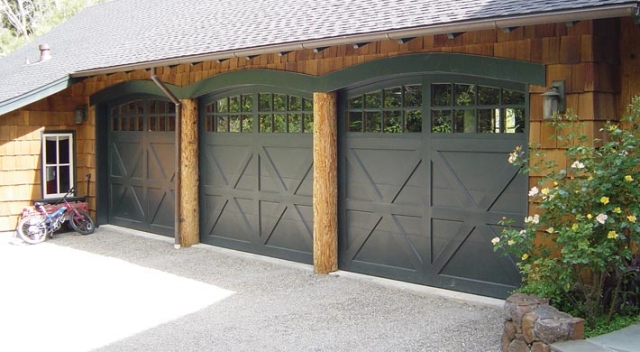 Three dark carriage house garage doors with arched top on garage with cedar shake siding