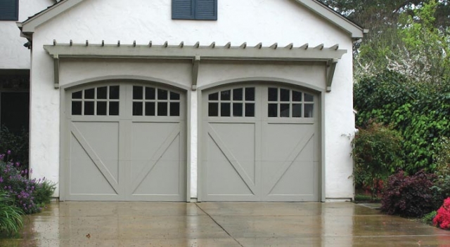 Two carriage house style garage doors on home with white stucco siding surrounded by lots of foliage