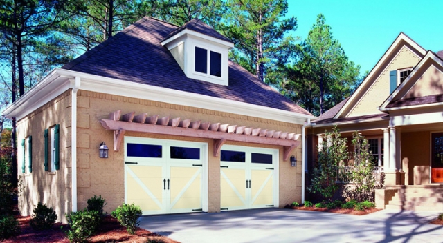 Suburban house with large tree in the background, separate garage has two carriage house garage doors