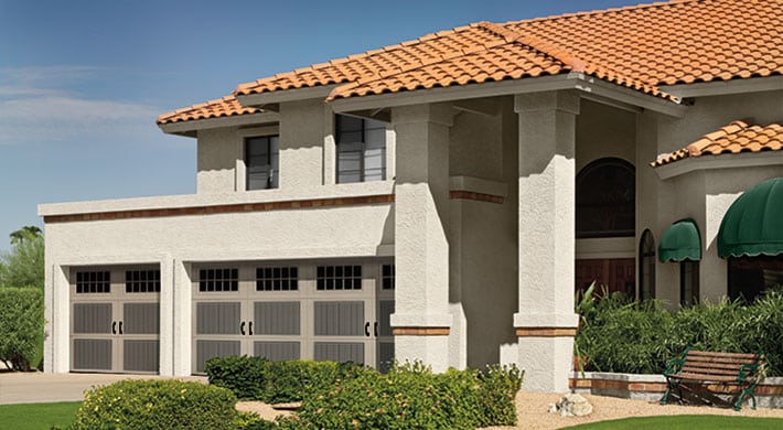 House with three car garage, dual color carriage house garage doors, stucco siding, and villa style tile roof