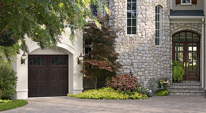 House with stucco and stone siding, elegant wood entrance door with similar wood tone carriage house garage door