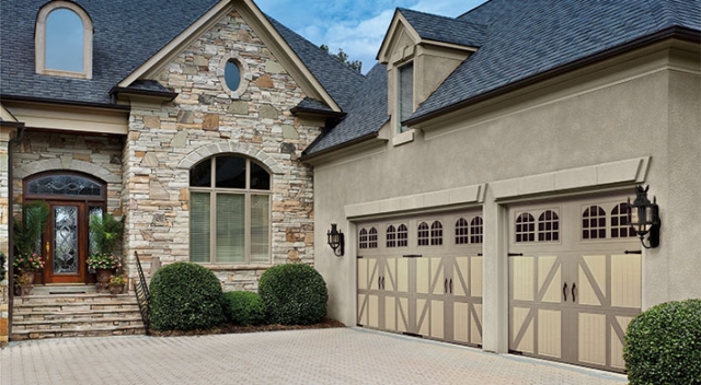 House with elegant front doors, stone and stucco siding, and three car garage with two carriage house style garage doors