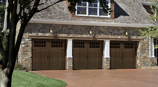 Three car garage with stone facade and divided by pilars, three carriage house style wood garage doors