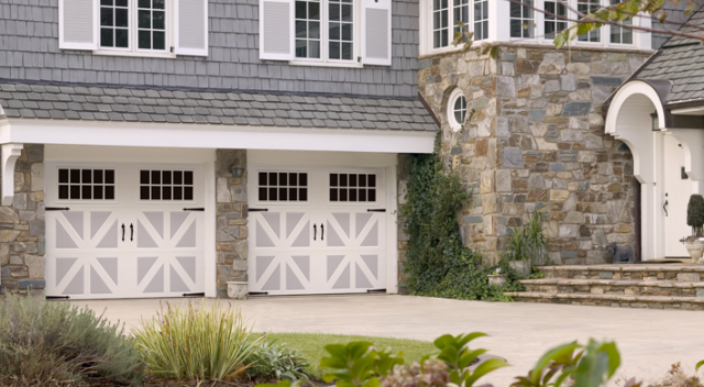 Two carriage house garage doors on two story home with gray shingle siding and mixed texture stone siding