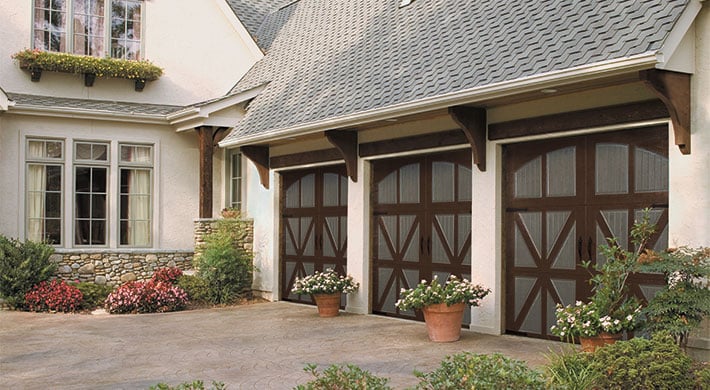 Two story house with stucco siding and stone and wood accents, three garage doors with custom finish