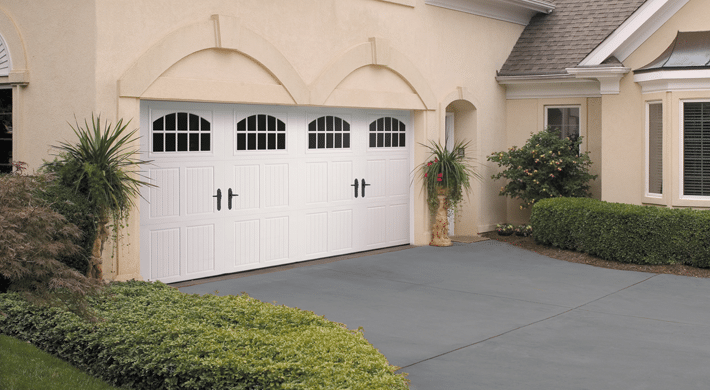 White Tuscany style garage doors with windows on house with neutral color stucco siding