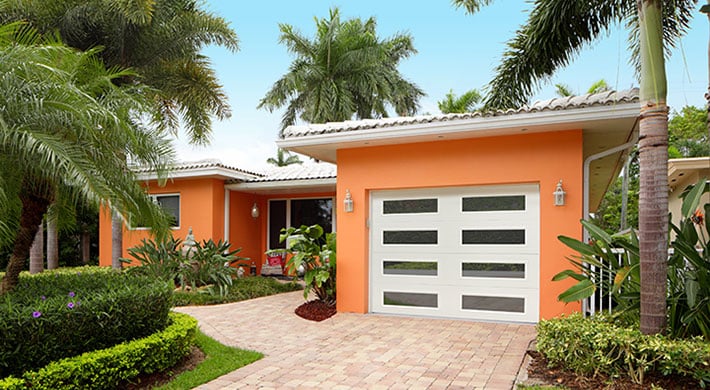 Bright orange house with one car garage, paver driveway, and tropical landscaping