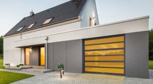 Modern home with light and dark gray stucco siding, paver stone driveway, and single-car specialty garage door