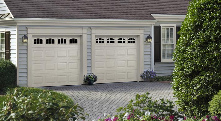 Two short panel garage doors on house with light blue siding and a paver patio