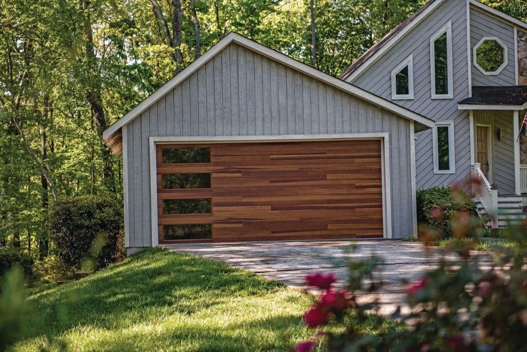 House with wood siding and CHI garage door with wood panels with glass windows on the left side of each panel. Image for CHI vs Clopay Garage Doors comparison.