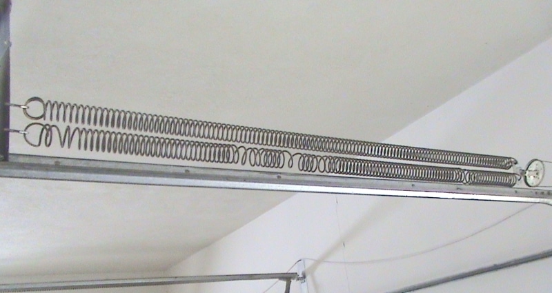 Photo of extension spring system with two springs on one side. The lower spring has visible warping. Image for post on can i just replace one spring?